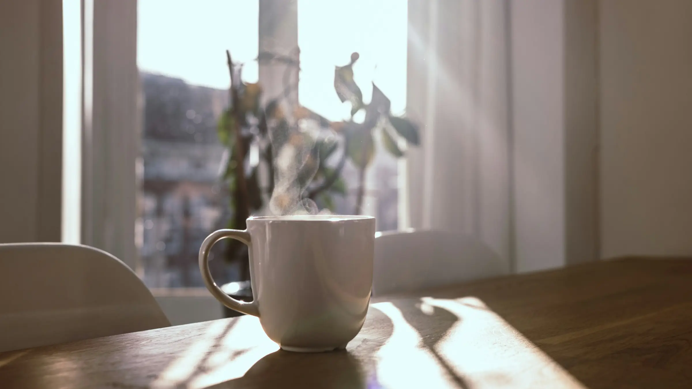 Taza humeante sobre la mesa de madera de una casa, junto a la ventana